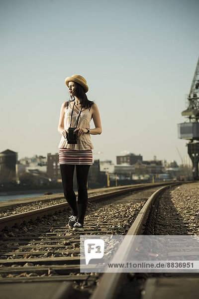 Young woman with old camera walking between rails