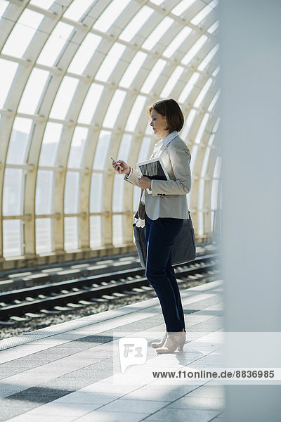 Geschäftsfrau mit Smartphone und Tablet-Computer wartet auf der Plattform