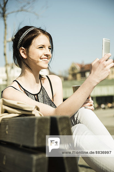 Portrait einer jungen Frau mit Kaffee zum Mitnehmen per Smartphone