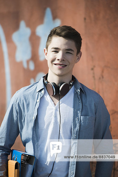 Portrait of smiling teenager with headphones and folders