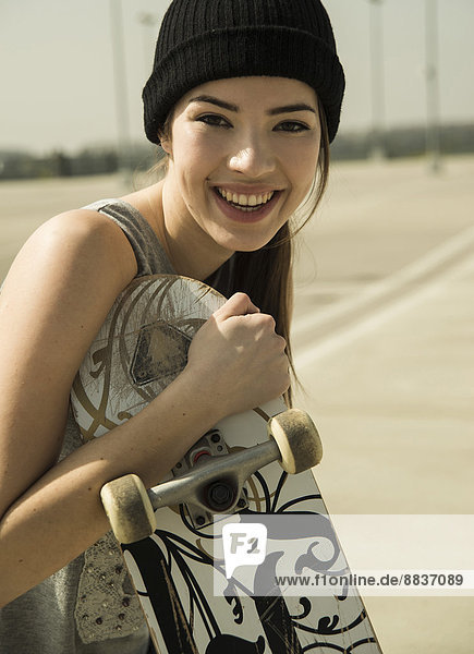 Porträt einer lächelnden jungen Frau mit Skateboard
