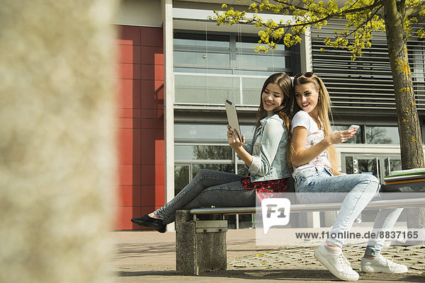 Zwei glückliche junge Frauen mit digitalem Tablett und Handy im Freien