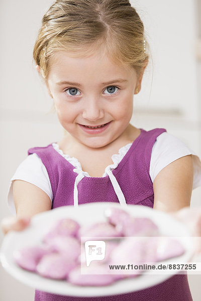 Porträt eines lächelnden kleinen Mädchens mit rosa Keksen