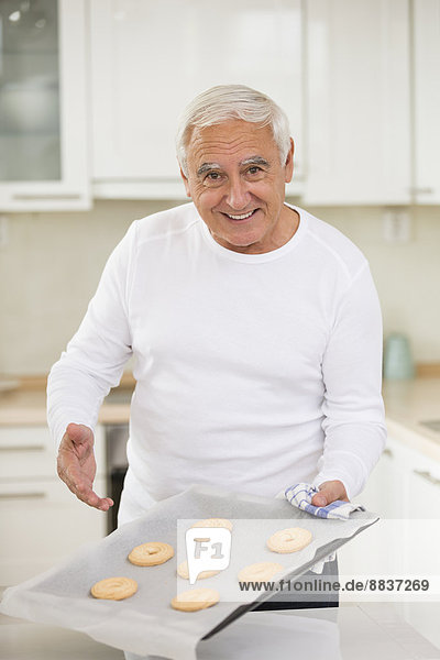 Senior Mann präsentiert selbstgebackene Kekse in seiner Küche