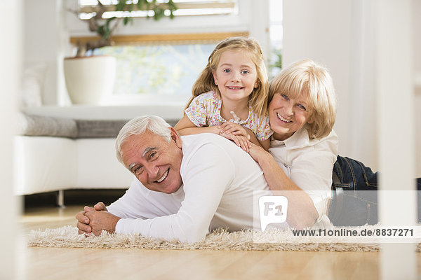 Familienporträt eines älteren Paares und einer Enkelin  die zu Hause auf dem Boden liegen.