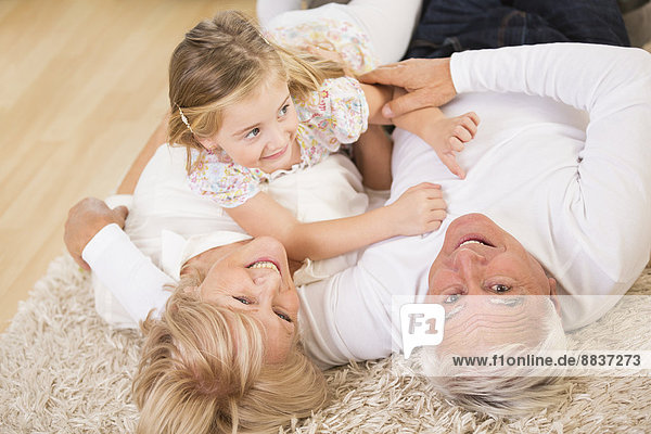 Seniorenpaar und Enkelin zu Hause auf dem Boden liegend