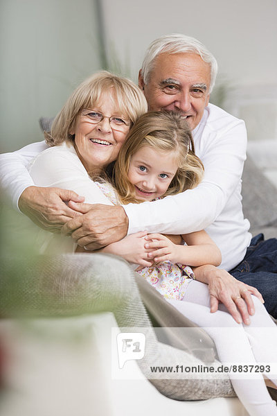 Porträt eines älteren Paares mit Enkelin auf Sofa im Wohnzimmer