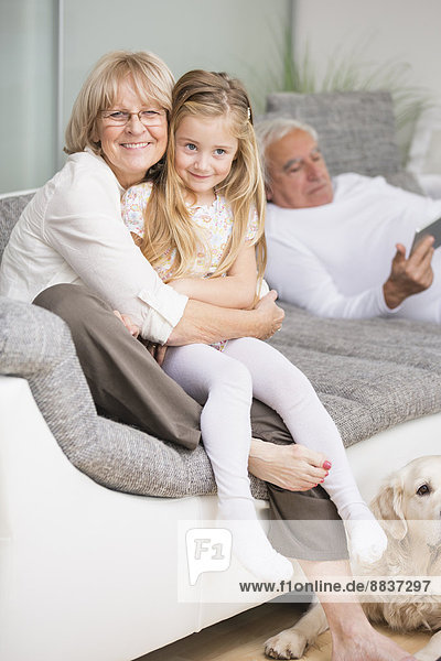Porträt einer älteren Frau  die ihre Enkelin auf dem Sofa im Wohnzimmer umarmt.