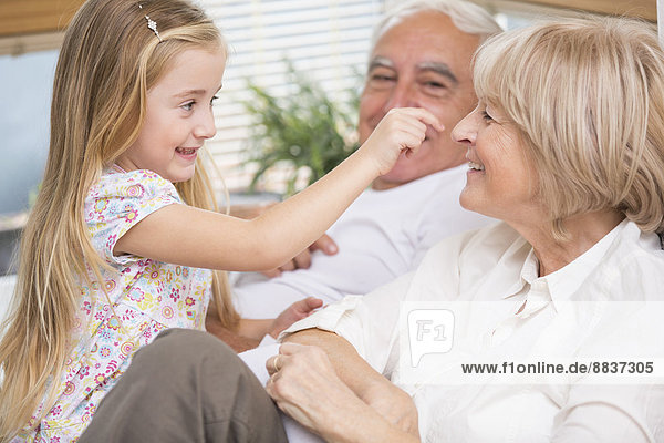 Senior couple and granddaughter relaxing on sofa in living room