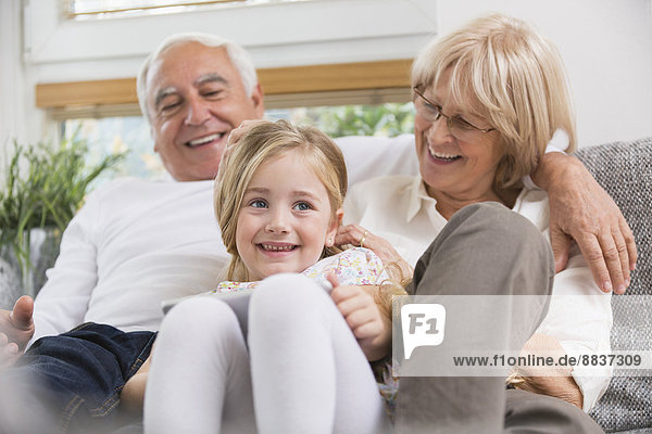 Senior couple and granddaughter sitting with digital tablet on sofa in living room