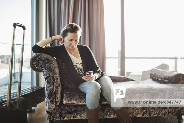 Geschäftsfrau mit Handy auf Chaiselongue im Hotelzimmer