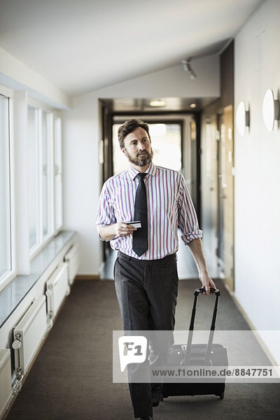 Businessman with suitcase walking in hotel corridor