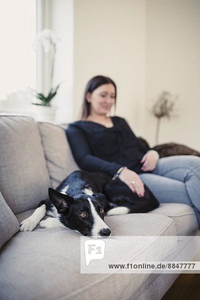 Frau sitzend mit Hund auf Sofa zu Hause
