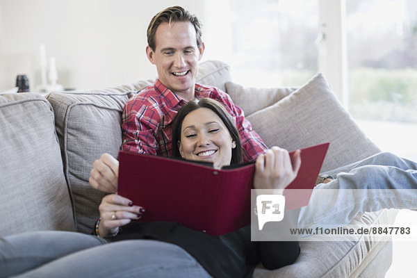 Glückliches Paar beim gemeinsamen Betrachten des Fotoalbums auf dem Sofa