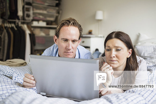 Paar mit Laptop im Bett zu Hause liegend