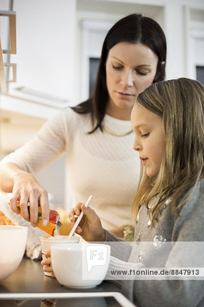 Mutter und Tochter fügen Geschmack in Tasse in der Küche hinzu