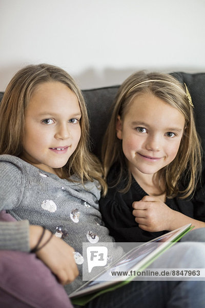 Porträt der Schwestern mit digitalem Tablett zum Entspannen auf dem Sofa