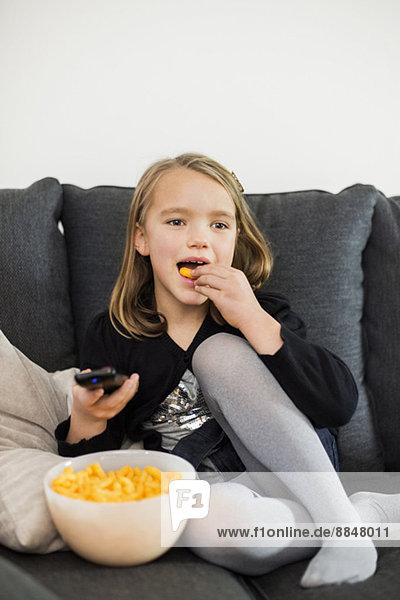 Mädchen essen Snacks,  während sie zu Hause auf dem Sofa fernsehen.