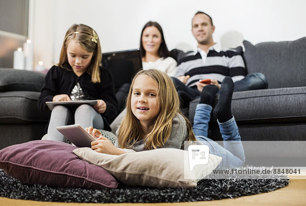 Portrait of girl holding digital tablet with family in living room