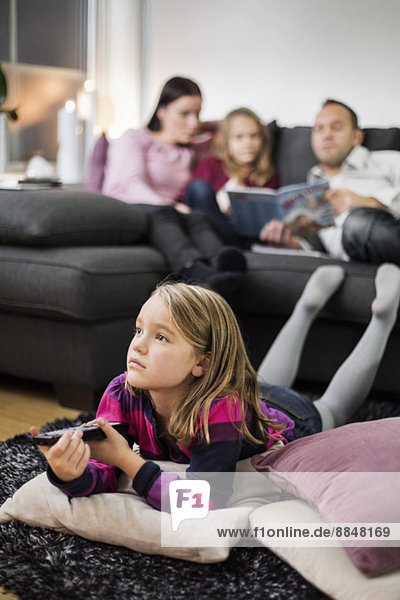 Mädchen beim Fernsehen auf dem Boden mit Familie im Hintergrund