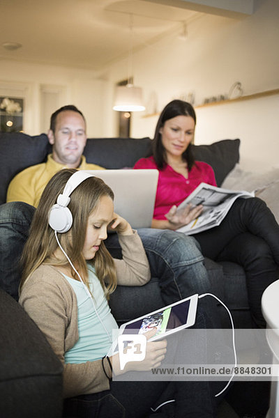 Mädchen hört Musik auf digitalem Tablett mit Eltern im Hintergrund zu Hause