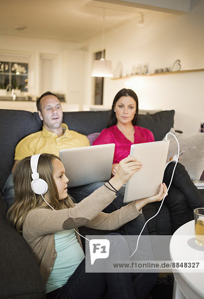 Girl showing digital tablet to parents in living room