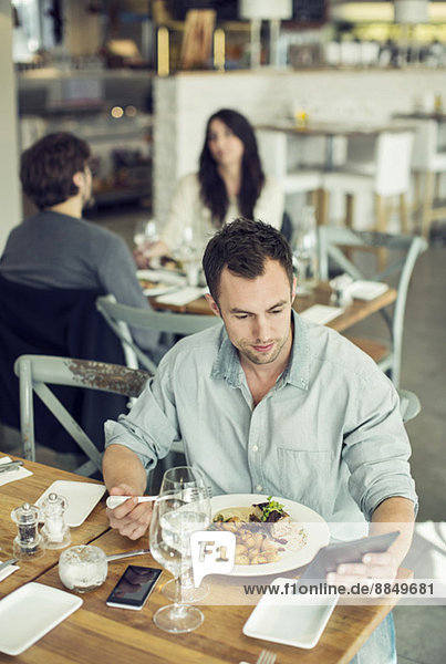 Mittlerer erwachsener Geschäftsmann mit digitalem Tablett beim Mittagessen im Restaurant