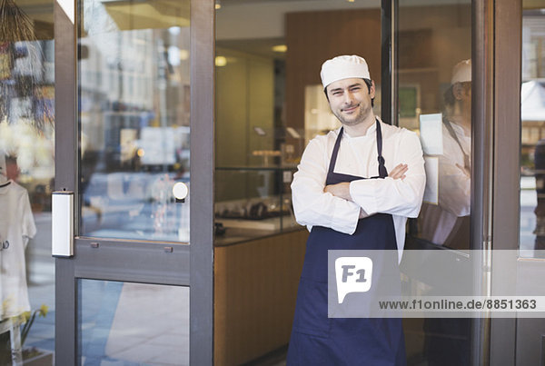 Portrait of confident owner standing with arms crossed at cafe entrance