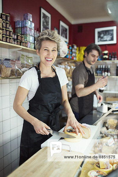 Porträt der glücklichen Verkäuferin beim Käseschneiden an der Theke im Supermarkt