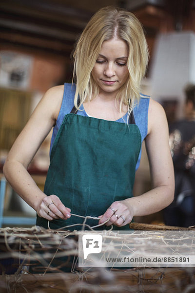 Junge blonde Arbeiterin beim Binden des Seils bei der Herstellung der Chaiselongue in der Werkstatt