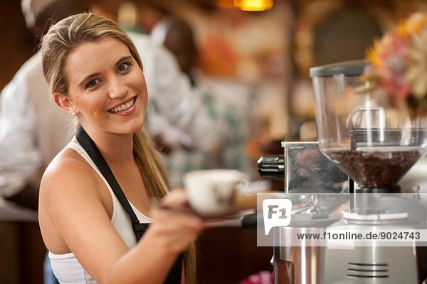 Porträt einer jungen Frau bei der Zubereitung einer Tasse Kaffee im Cafe