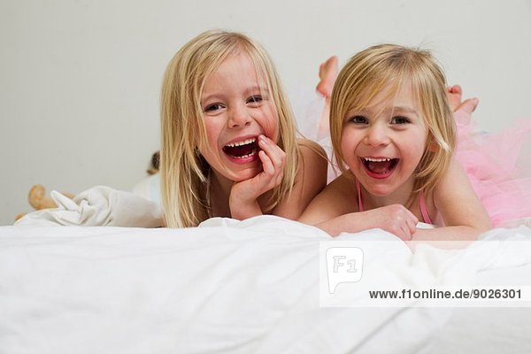 Portrait of two young sisters lying on front in bed