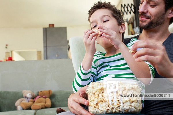 Vater und Sohn teilen sich Popcorn im Wohnzimmer
