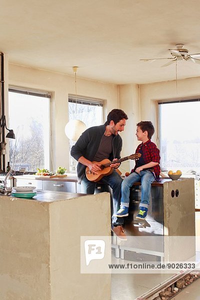 Father and young son playing guitar in kitchen