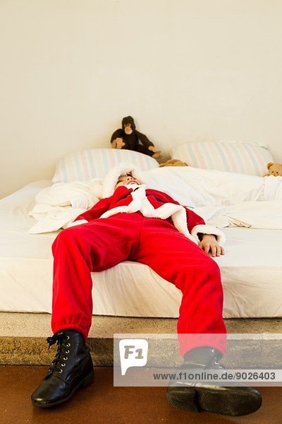 Kleiner Junge verkleidet als Weihnachtsmann auf dem Bett liegend