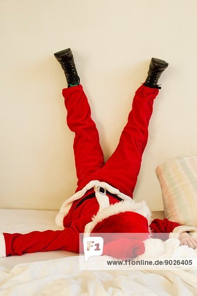 Kleiner Junge verkleidet als Weihnachtsmann auf Bett mit erhobenen Beinen