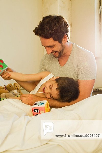 Father and young son playing on bed