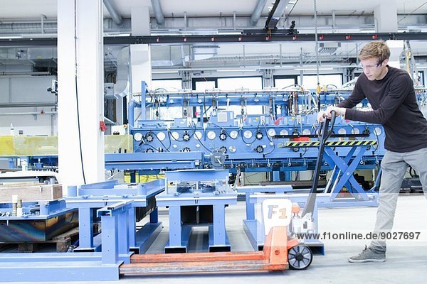 Mid adult male moving products on pallet jack in engineering plant