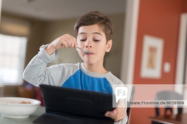 Junge schaut beim Frühstück auf das digitale Tablett