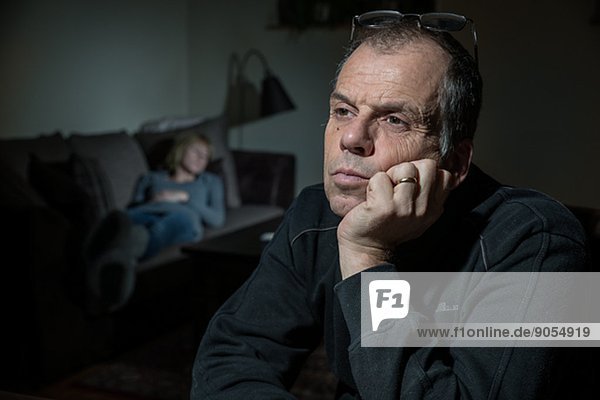 Mature man looking away woman on sofa on background