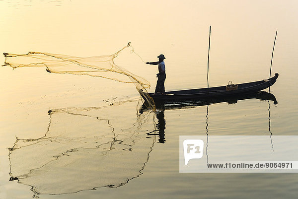 Fisherman in a boat tossing out a net morning light Thaungthaman Lake Amarapura Mandalay Division Myanmar