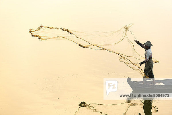 Fisherman in a boat tossing out a net morning light Thaungthaman Lake Amarapura Mandalay Division Myanmar