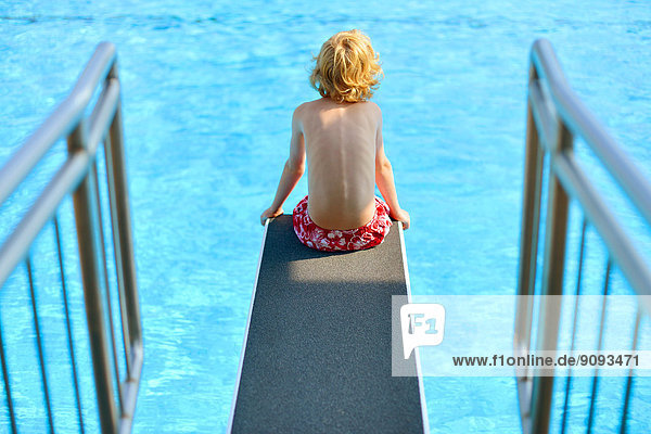 Ein Junge sitzt auf dem drei Meter Brett eines Freibades.