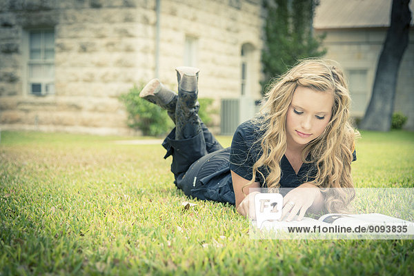 Porträt einer jungen Frau  die auf Gras liegt und ein Buch liest.
