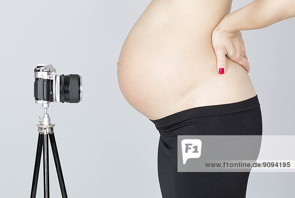 Nackter Bauch der schwangeren Frau gegenüber der alten Kamera auf Stativ