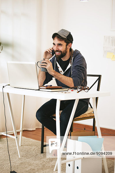 Porträt eines Mannes beim Telefonieren mit dem Smartphone im modernen Home Office