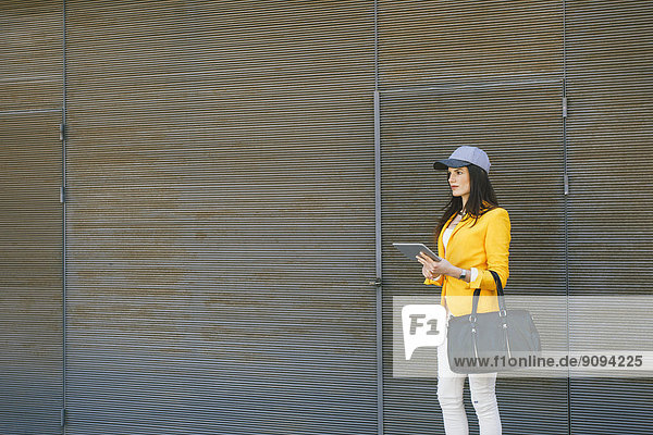 Spanien,  Katalonien,  Barcelona,  junge moderne Frau mit gelber Jacke und Tablet-Computer wartend