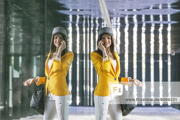 Spanien  Katalonien  Barcelona  lächelnde junge Frau mit gelber Jacke in Glasfassade reflektierend