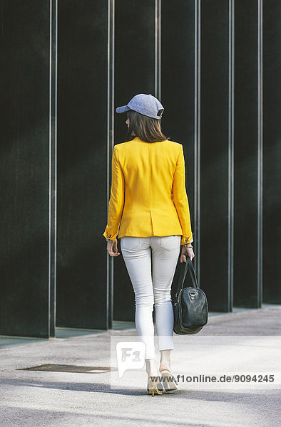 Spanien Catalunya  Barcelona  junge moderne Frau mit gelber Jacke unterwegs  Blick von hinten