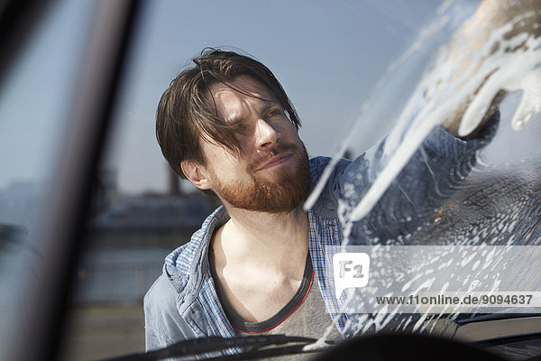 Mann wäscht Frontscheibe eines Autos